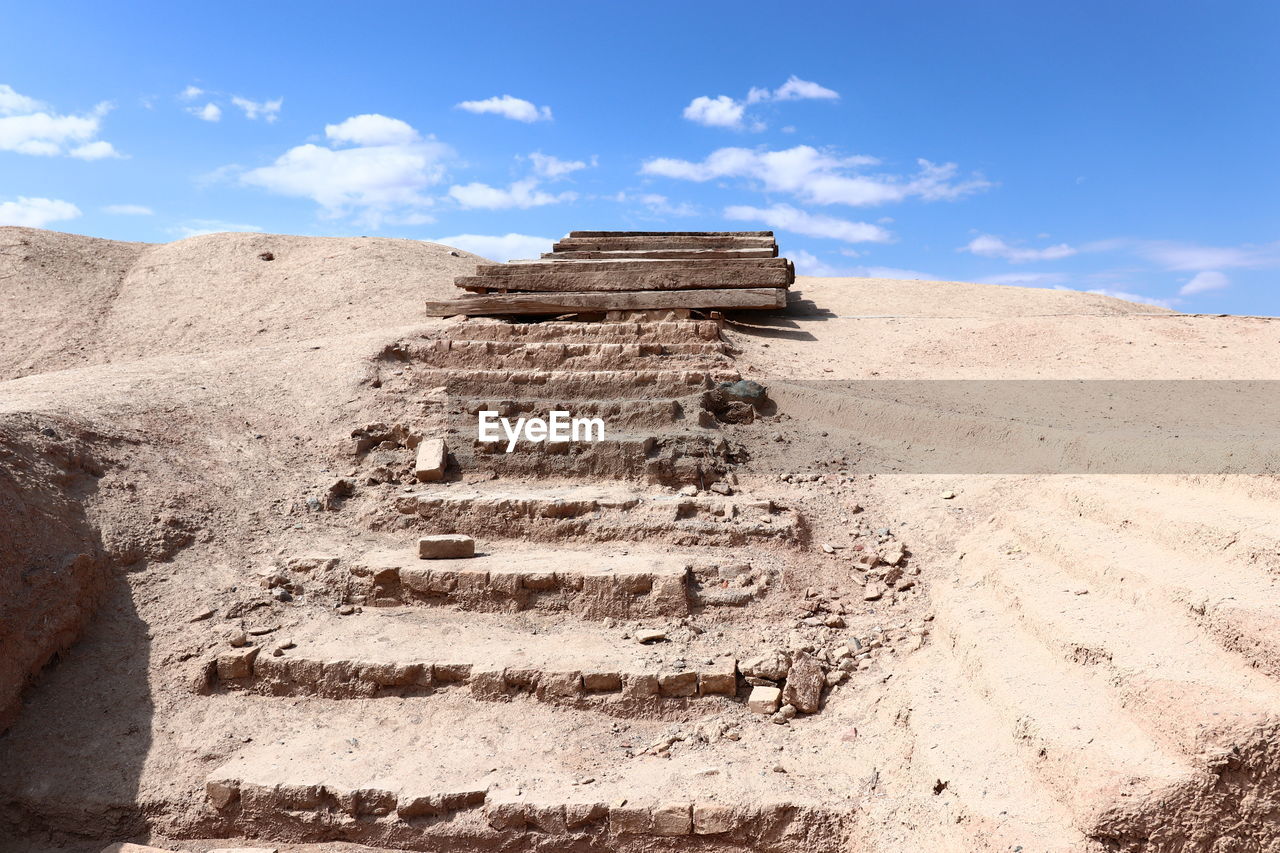 sky, land, monument, landscape, ancient, nature, history, cloud, architecture, travel, travel destinations, the past, environment, ancient history, desert, sand, rock, scenics - nature, blue, staircase, no people, temple, wadi, geology, archaeological site, tourism, climate, outdoors, day, ancient civilization, built structure, ruins, sunlight, natural environment, archaeology, non-urban scene, old ruin, soil, arid climate, sunny, tranquility