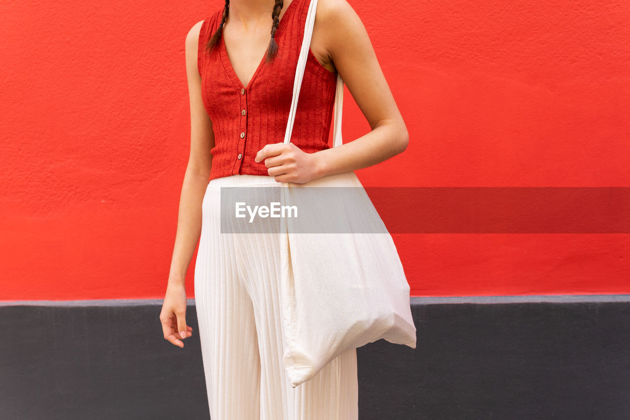 Crop view of anonymous trendy female with eco friendly textile bag standing on street near red building in city