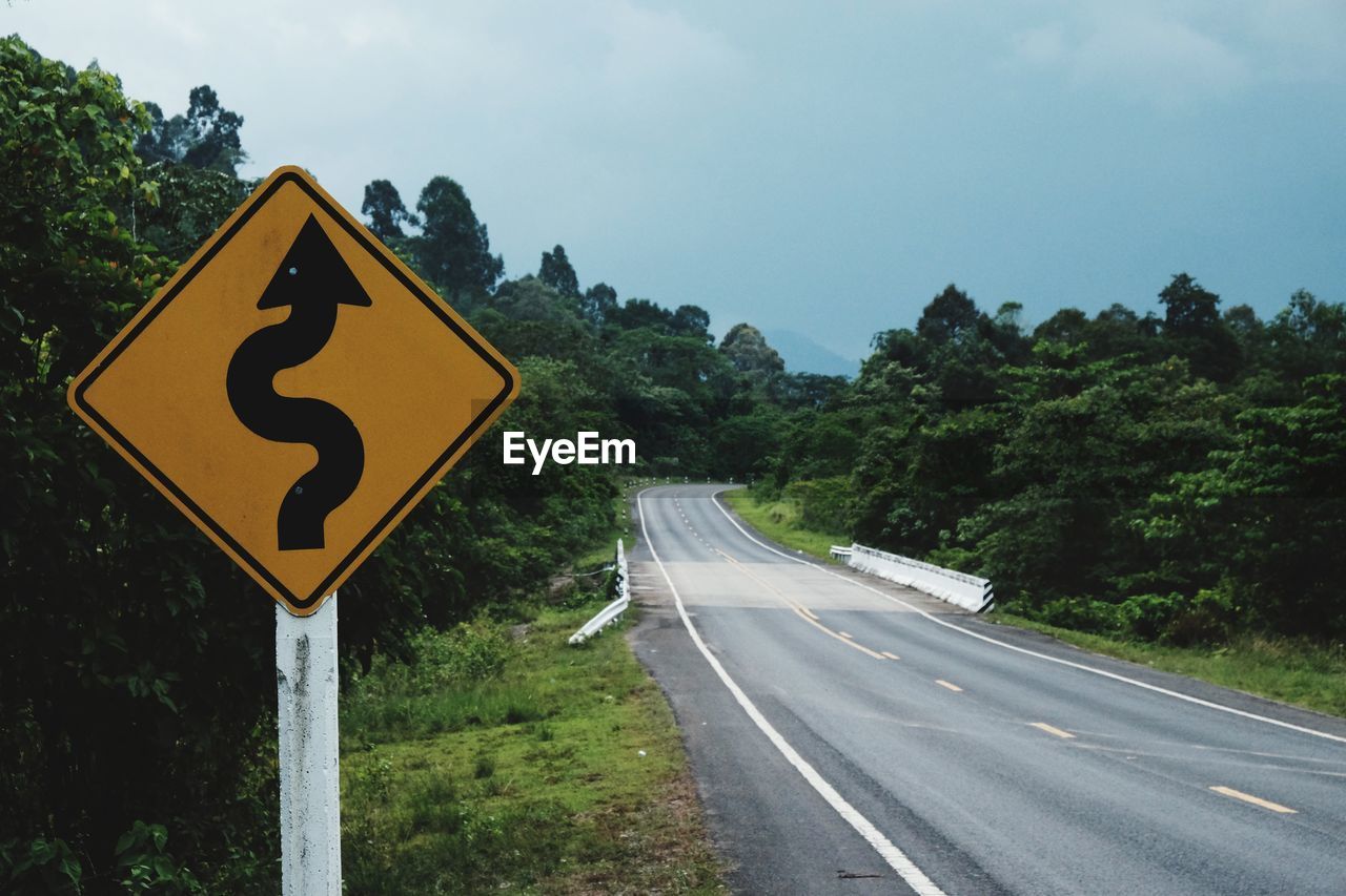 Road sign by street against sky