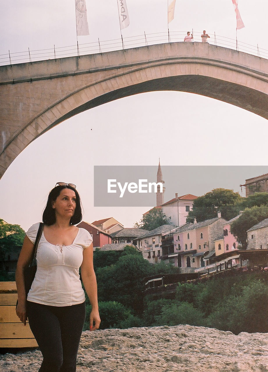 Portrait of woman standing against bridge in city