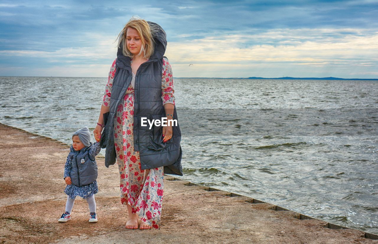 WOMEN STANDING ON SEA SHORE AGAINST SKY