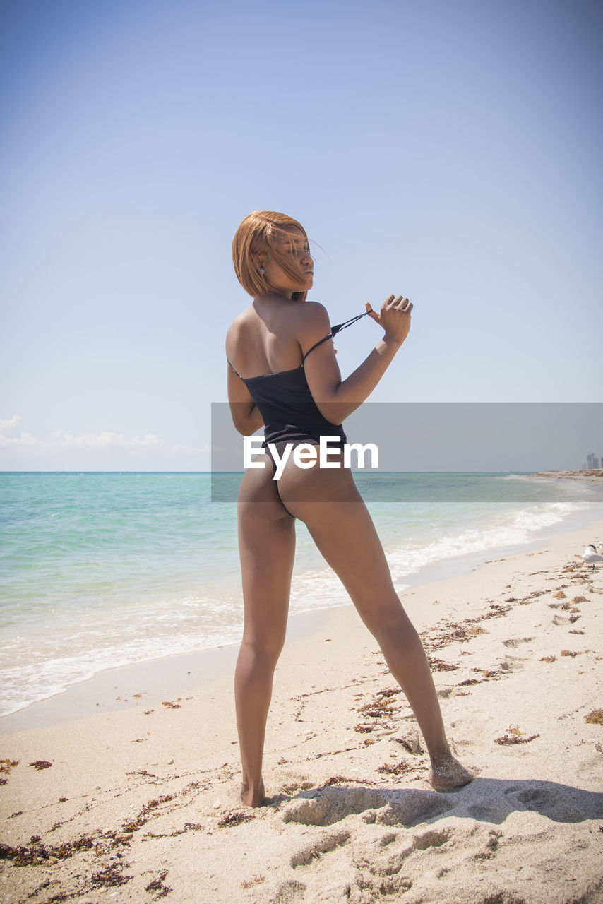 land, beach, sea, one person, adult, water, women, clothing, sky, nature, holiday, sand, full length, vacation, trip, leisure activity, swimwear, summer, lifestyles, young adult, bikini, relaxation, female, blond hair, human leg, sunlight, beauty in nature, body of water, horizon over water, copy space, photo shoot, exercising, day, limb, sports, sun tanning, standing, horizon, person, hairstyle, motion, tranquility, wellbeing, travel, blue, happiness, sunny, enjoyment, outdoors, clear sky, emotion, smiling, vitality, child, childhood, activity, carefree, fashion, idyllic