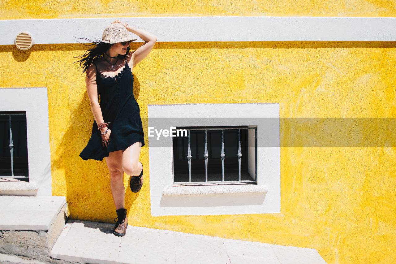 Full length of young woman standing leaning on yellow wall