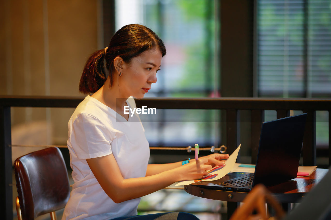 YOUNG WOMAN USING MOBILE PHONE IN OFFICE