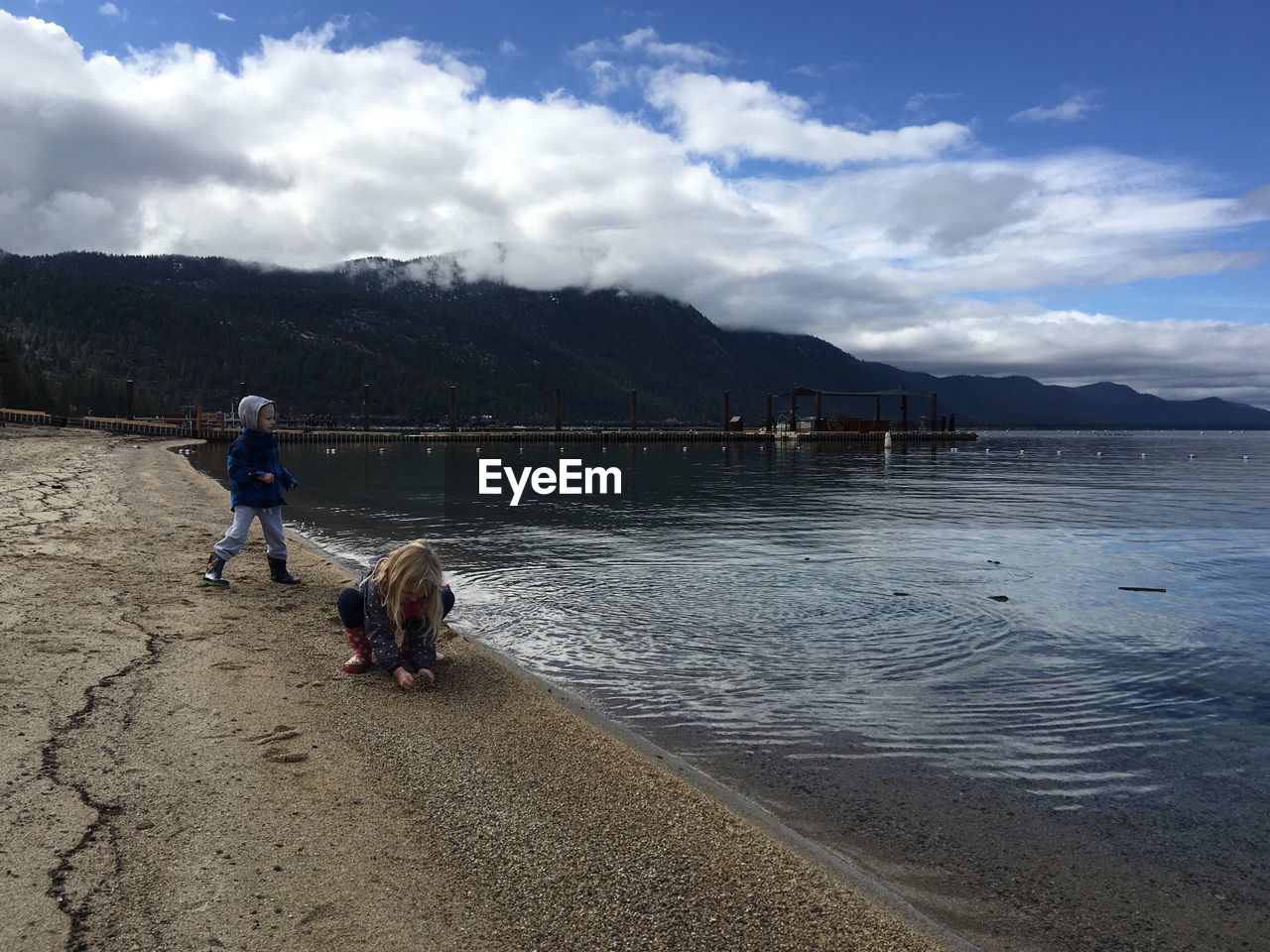 Children playing by lake tahoe against cloudy sky