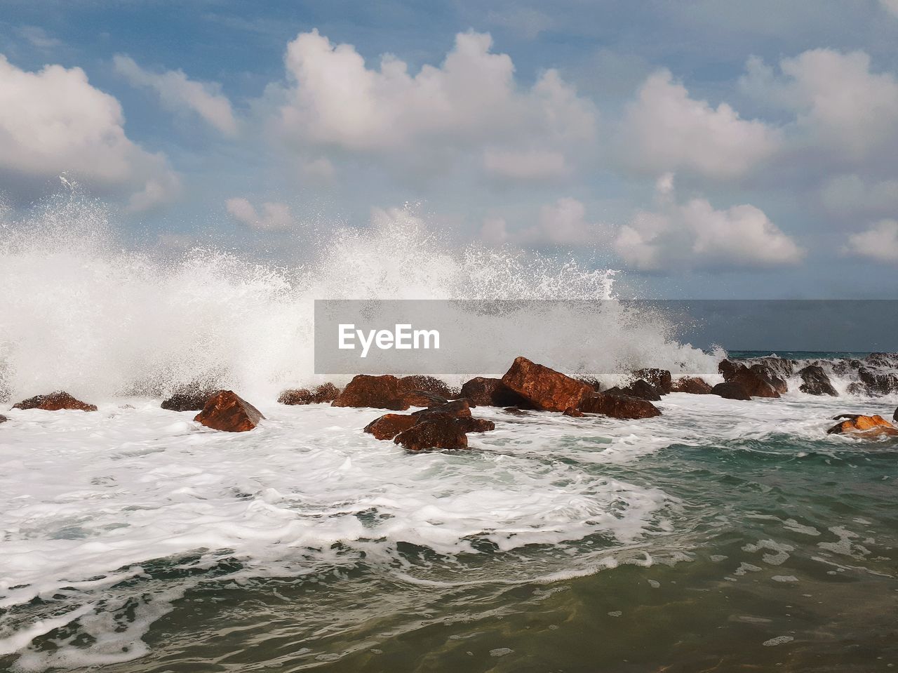 Waves splashing on rocks against sky