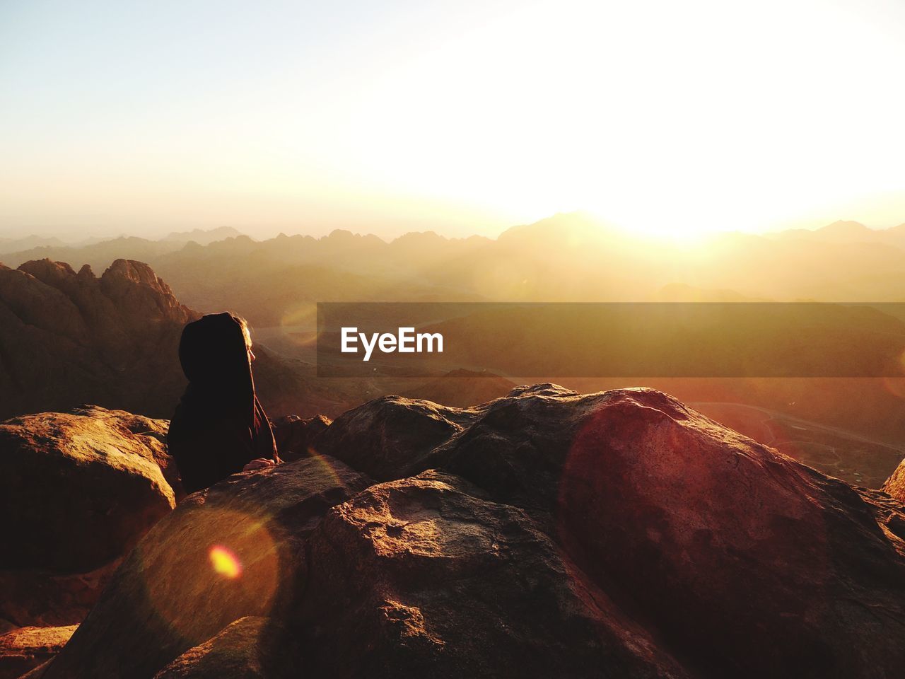 Woman by rocks against sky during sunrise