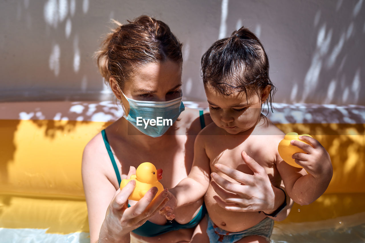 Young mother with a mask in an inflatable pool with her little daughter. safe holiday concept