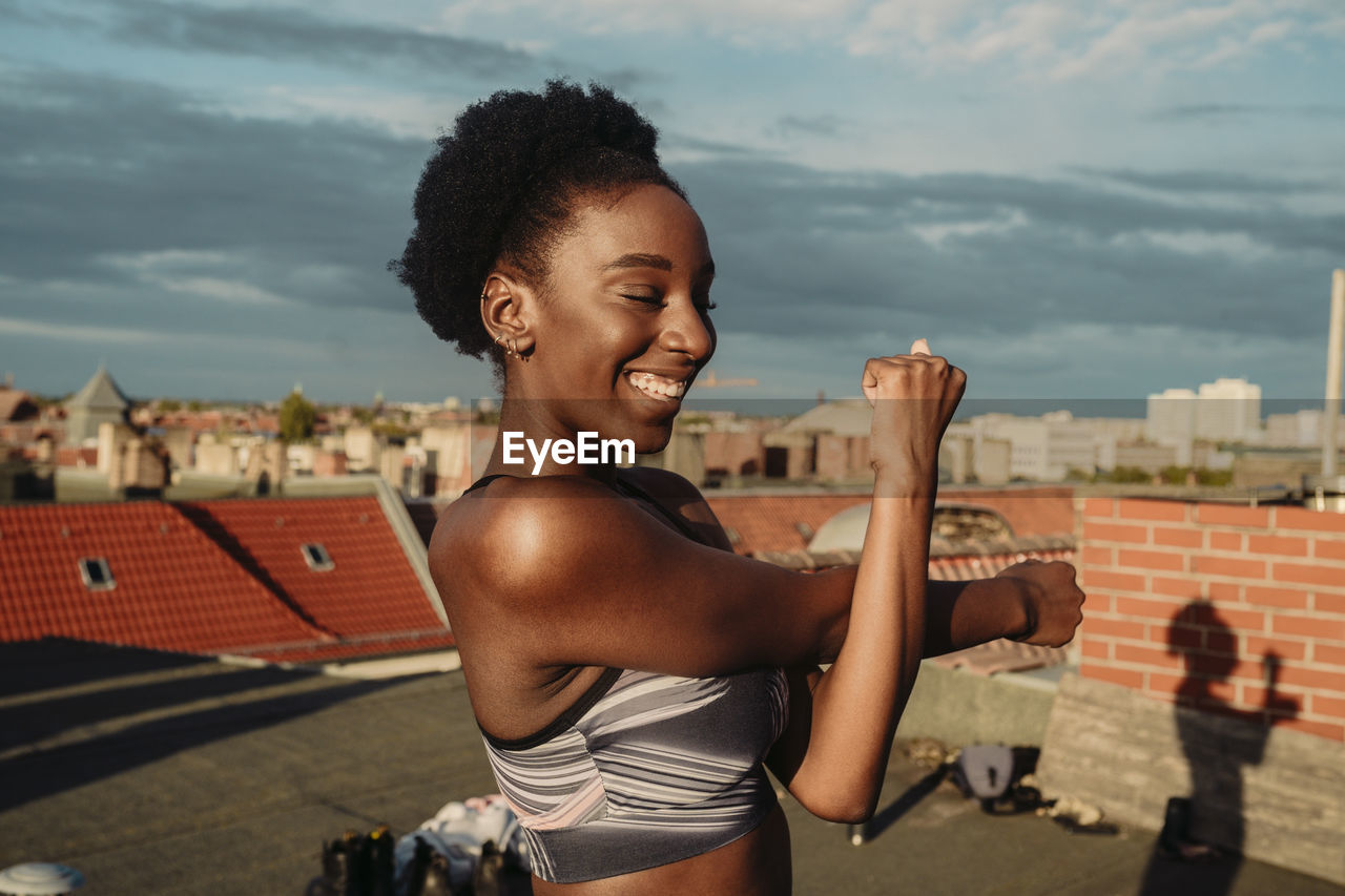 Smiling female stretching on rooftop during sunrise