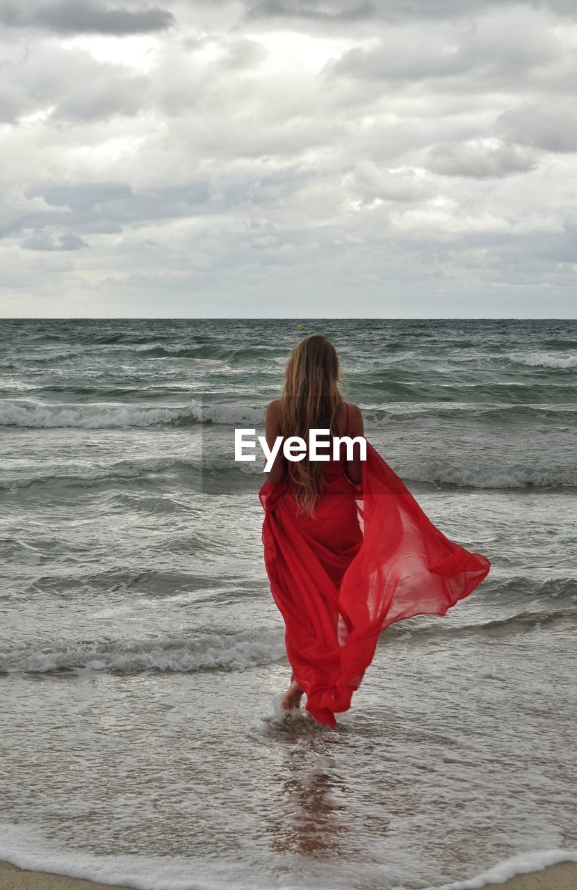 Rear view of woman walking on beach against sky