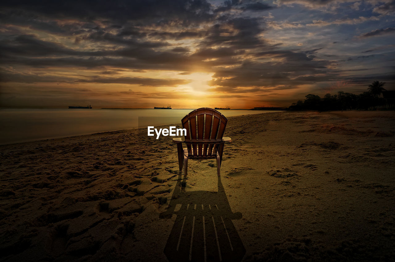 Deck chairs on beach against sky during sunset