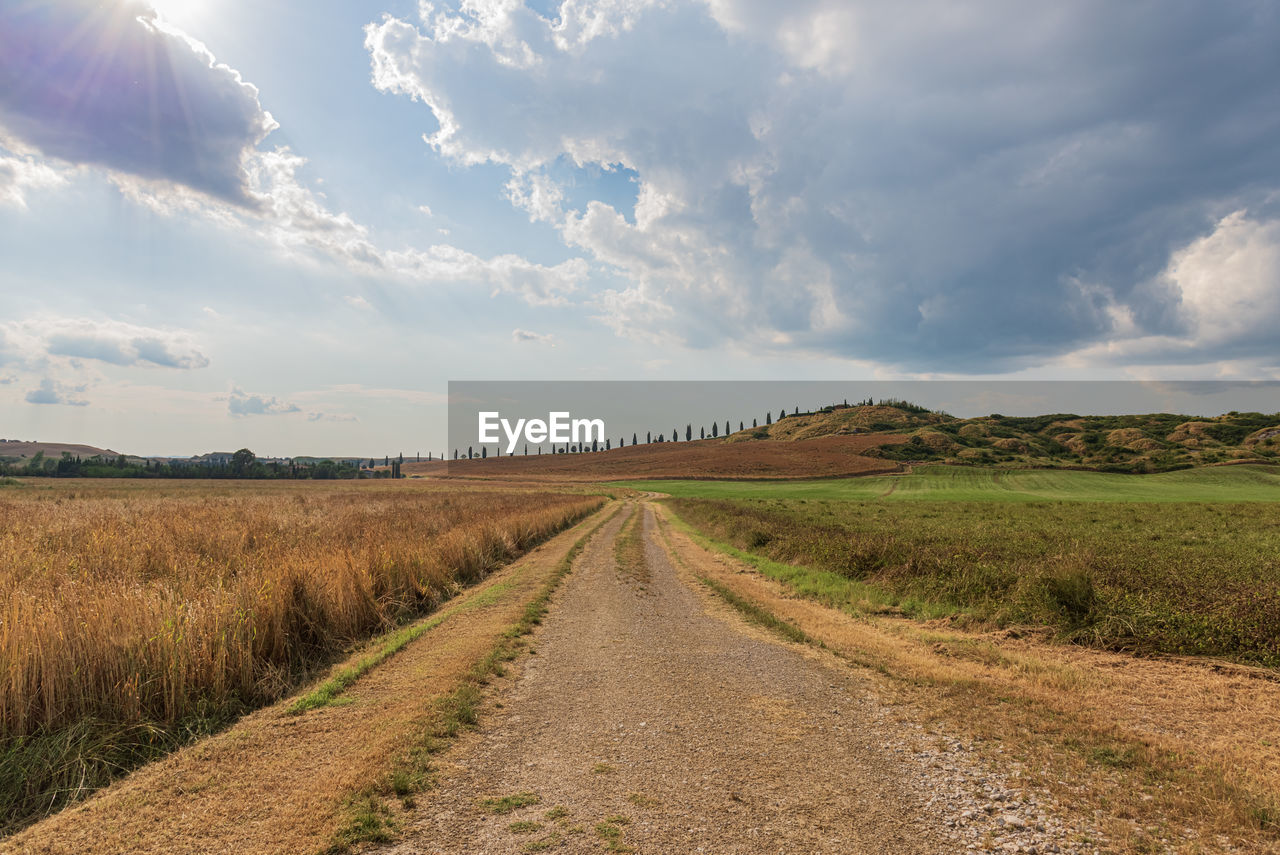 Dirt road amidst field against sky