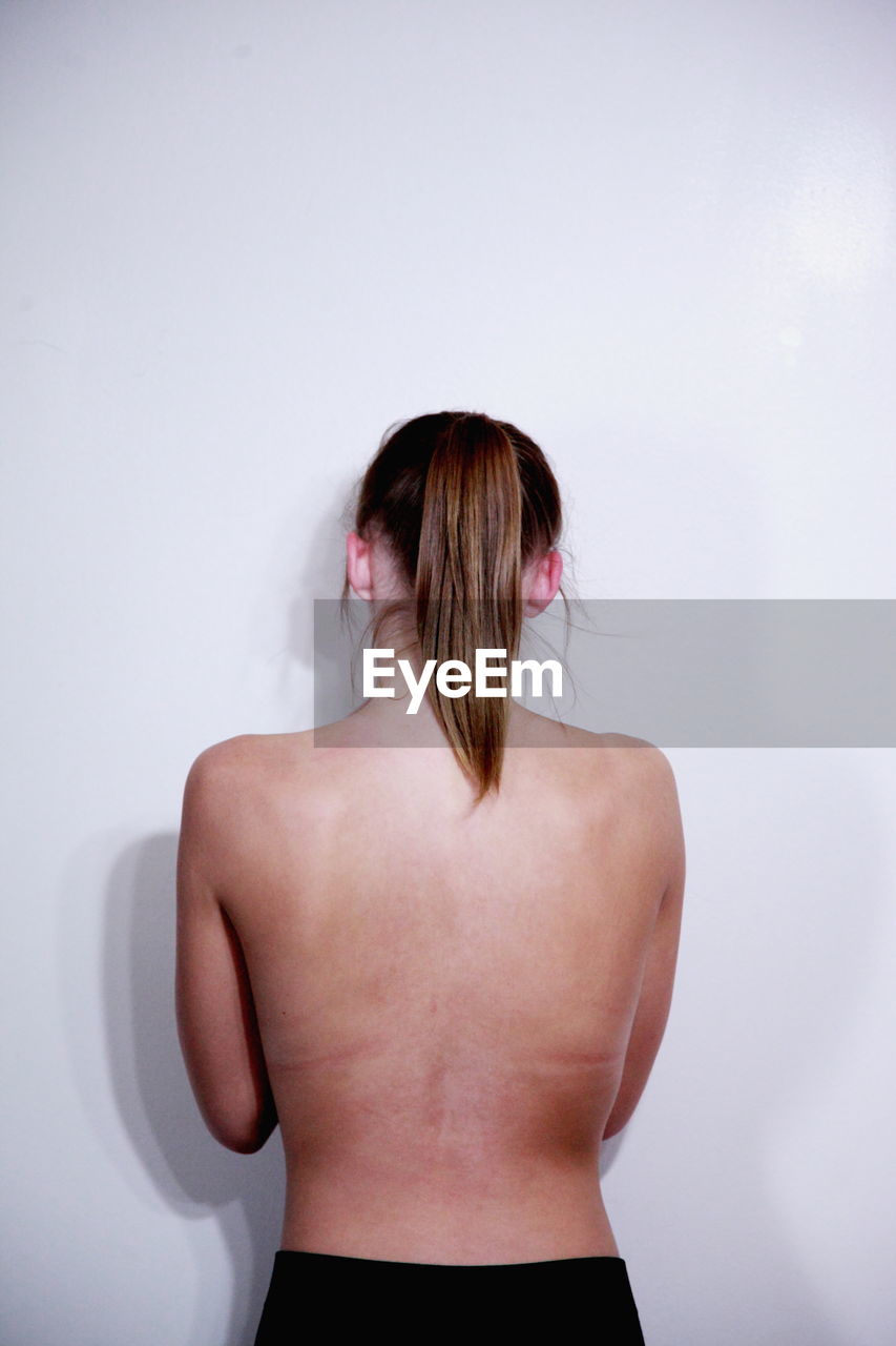 Rear view of topless woman standing against white background