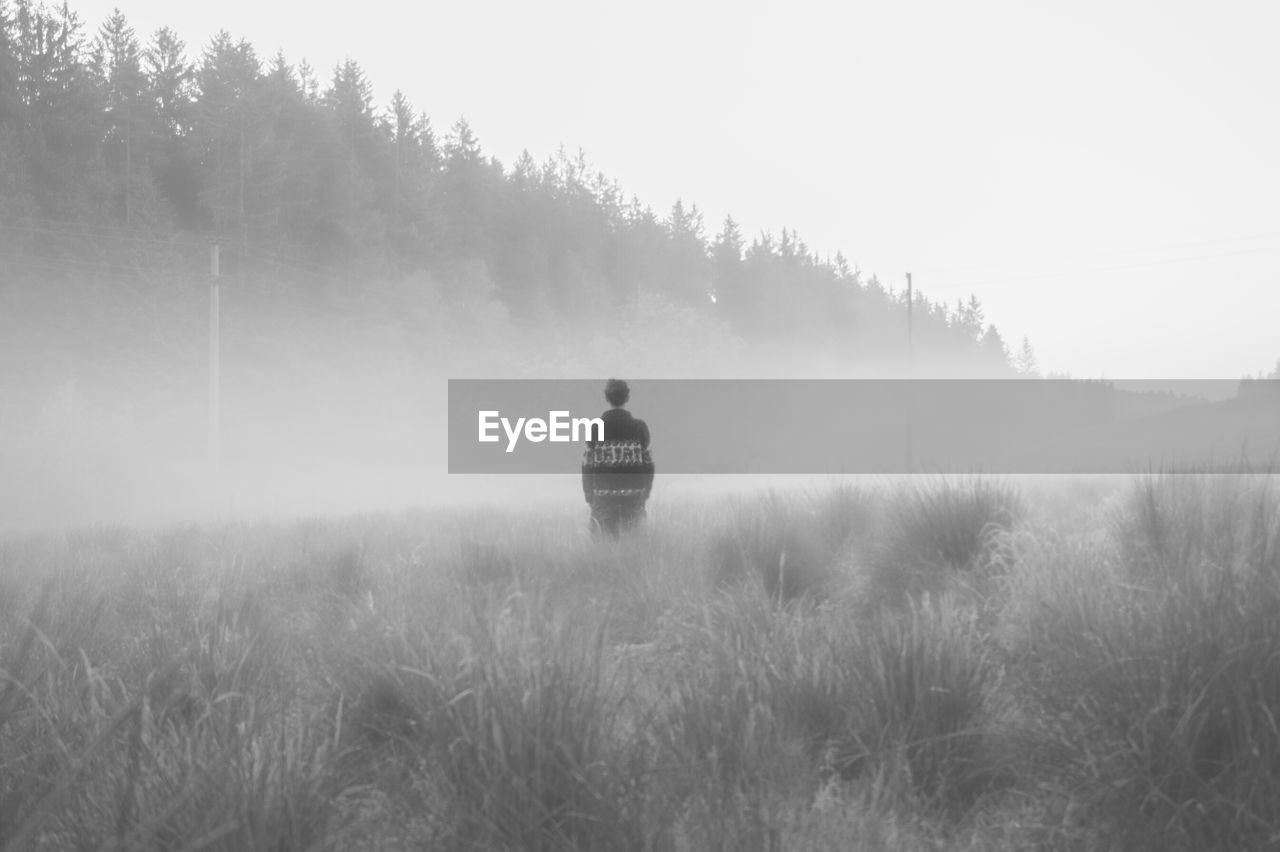 REAR VIEW OF MAN ON FIELD AGAINST SKY IN FOGGY WEATHER