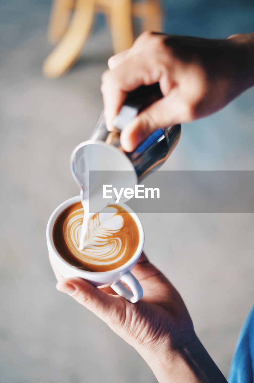 Close-up of hand making froth art in coffee