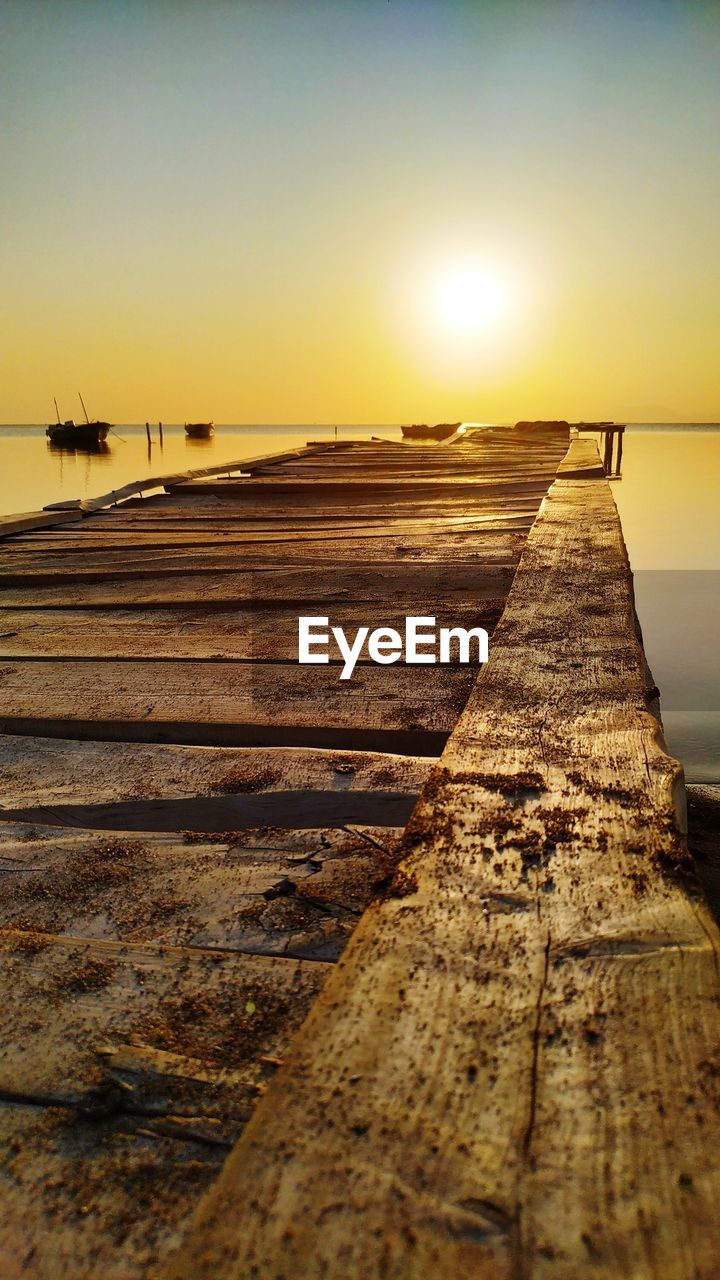 SURFACE LEVEL OF PIER ON BEACH AGAINST SKY DURING SUNSET