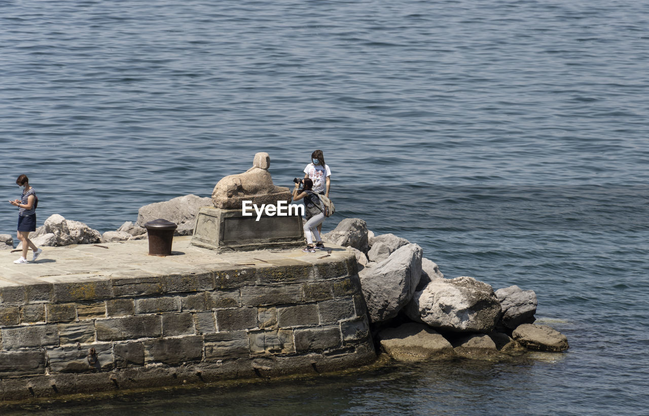 water, sea, rock, shore, nature, coast, day, men, sitting, lifestyles, leisure activity, outdoors, animal, animal themes, beauty in nature, full length, adult, animal wildlife, group of animals, ocean, wildlife, bird, bay, breakwater, group of people, relaxation, high angle view