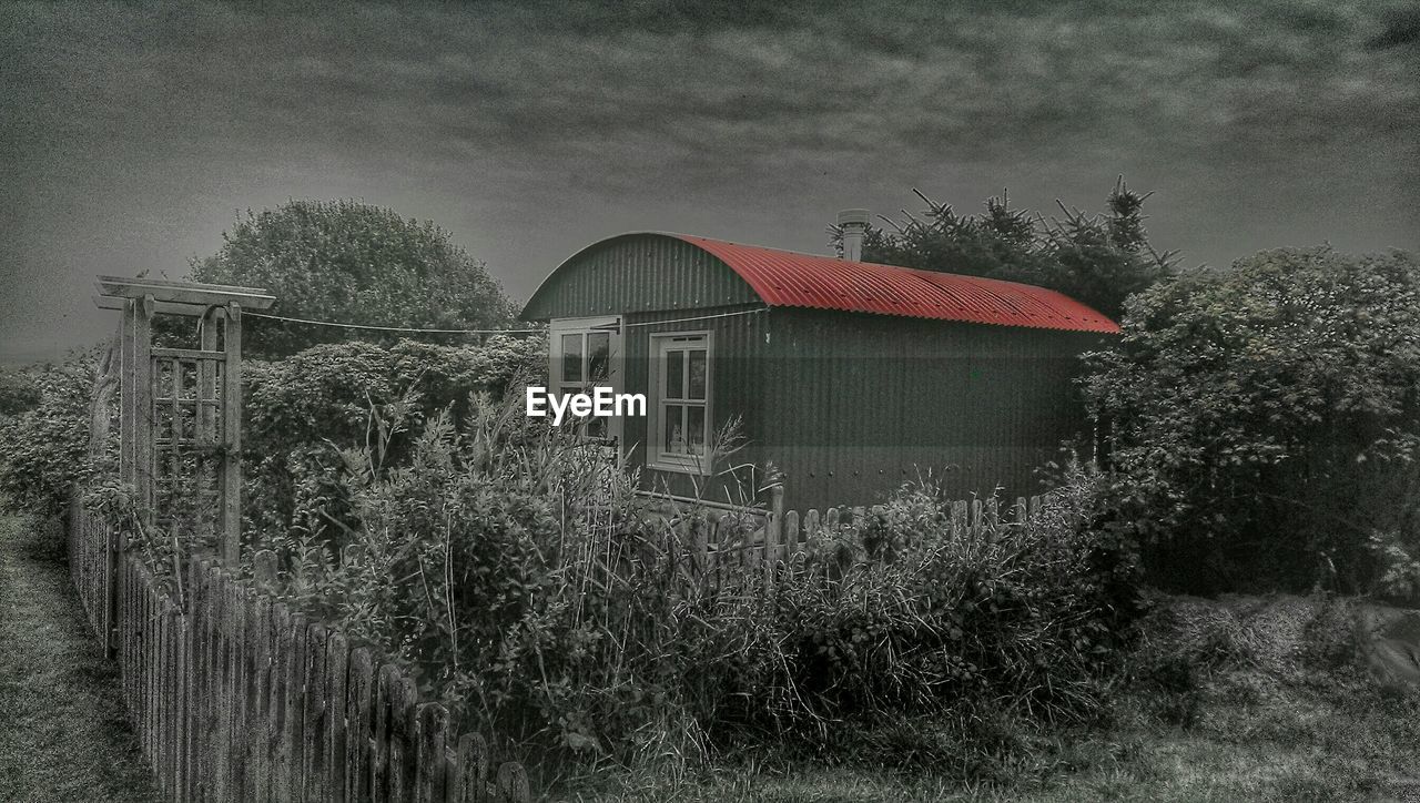 House on field by trees against sky