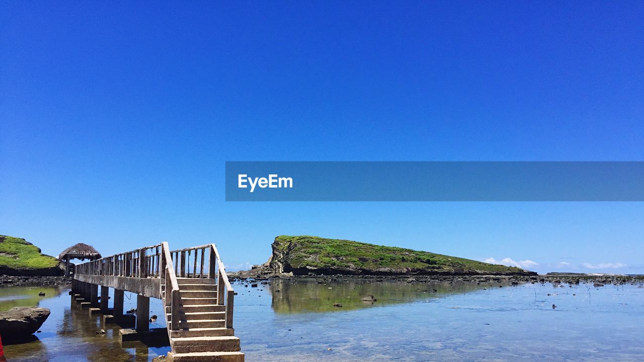 Pier over sea against clear blue sky