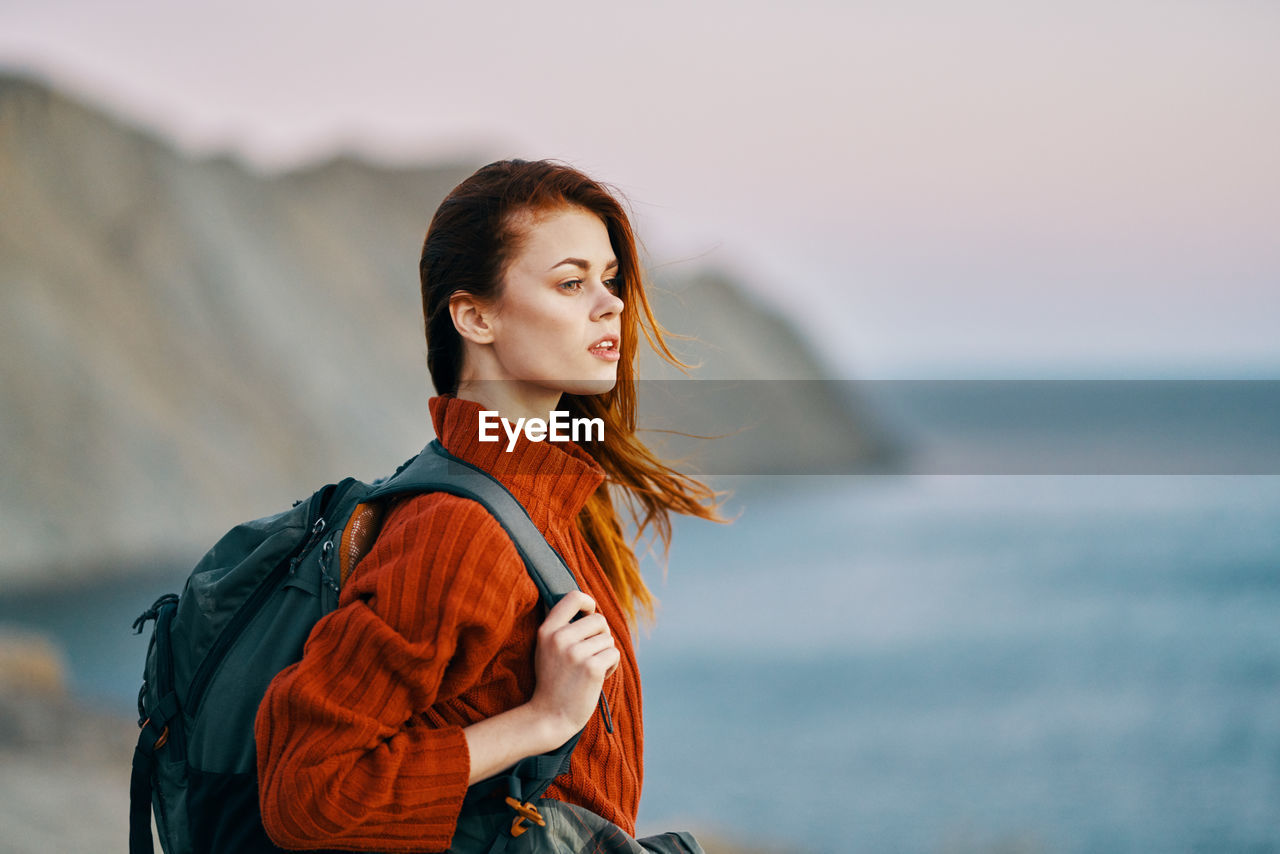 YOUNG WOMAN LOOKING AWAY AGAINST SEA