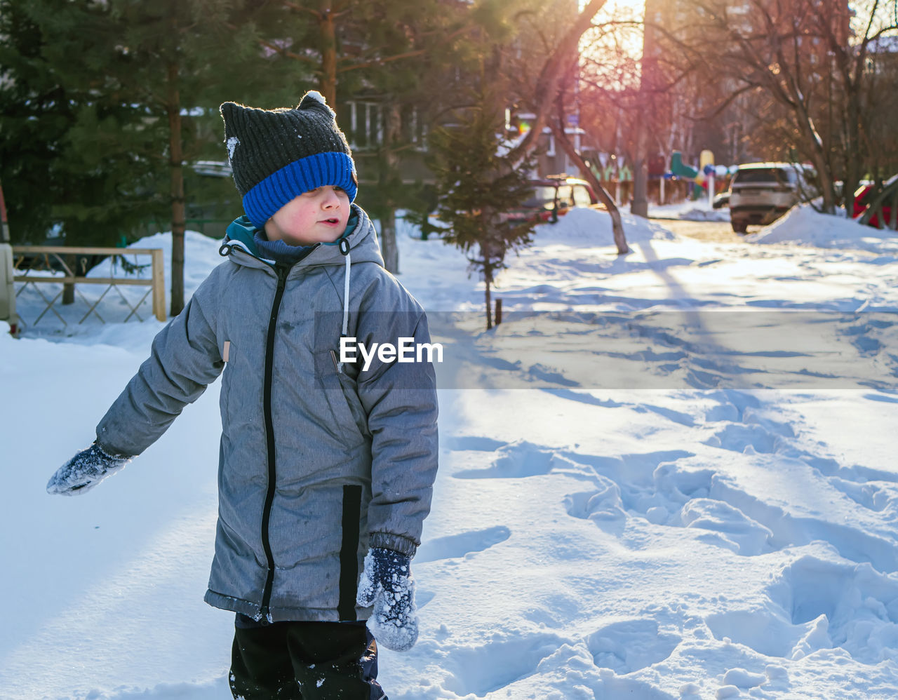 Smiling caucasian boy in green jacket and blue knit cap is standing on the snow.