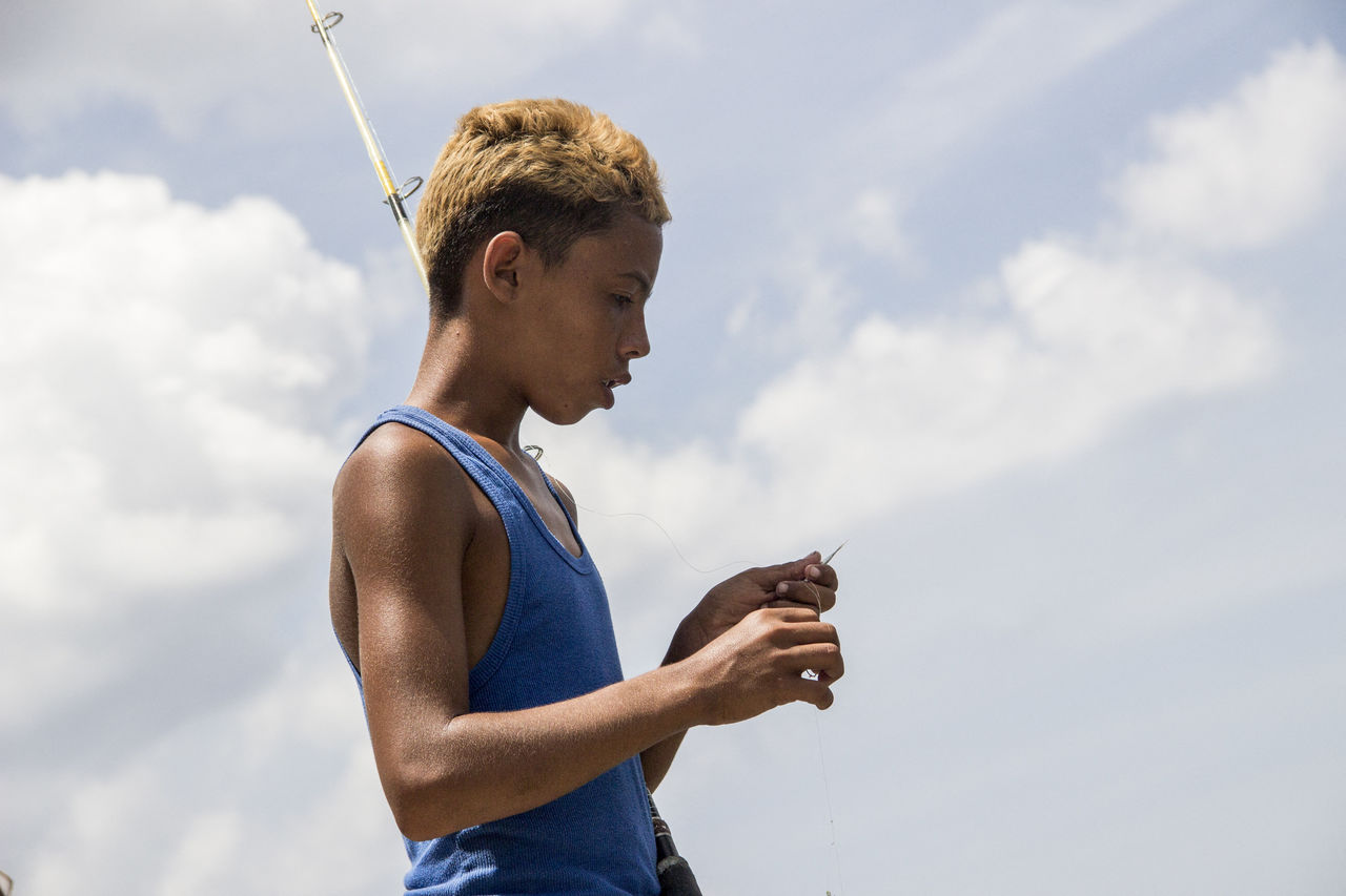 SIDE VIEW OF YOUNG MAN USING PHONE AGAINST SKY