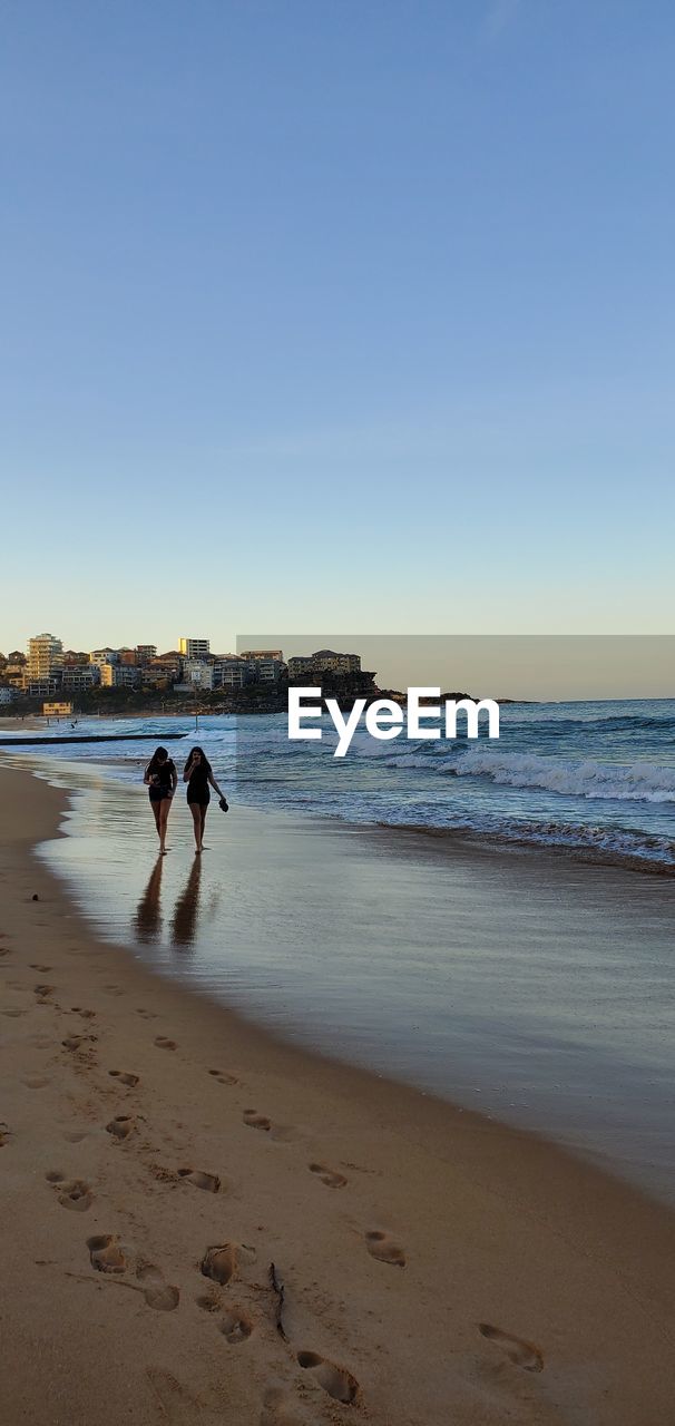 MEN ON BEACH AGAINST CLEAR SKY