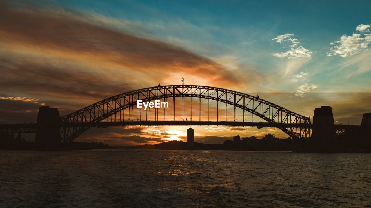 Silhouette bridge over river against sky during sunset