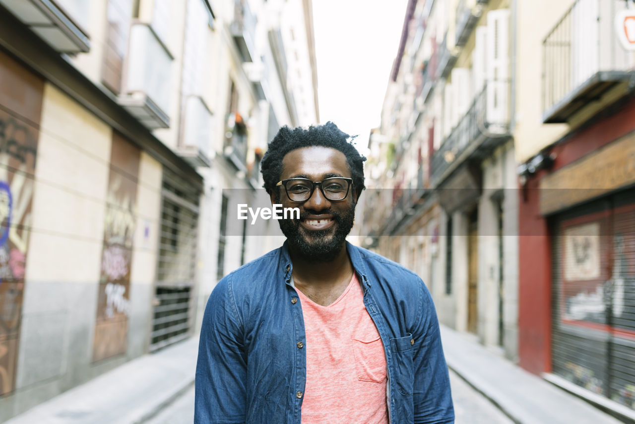 PORTRAIT OF SMILING YOUNG MAN STANDING AGAINST WALL