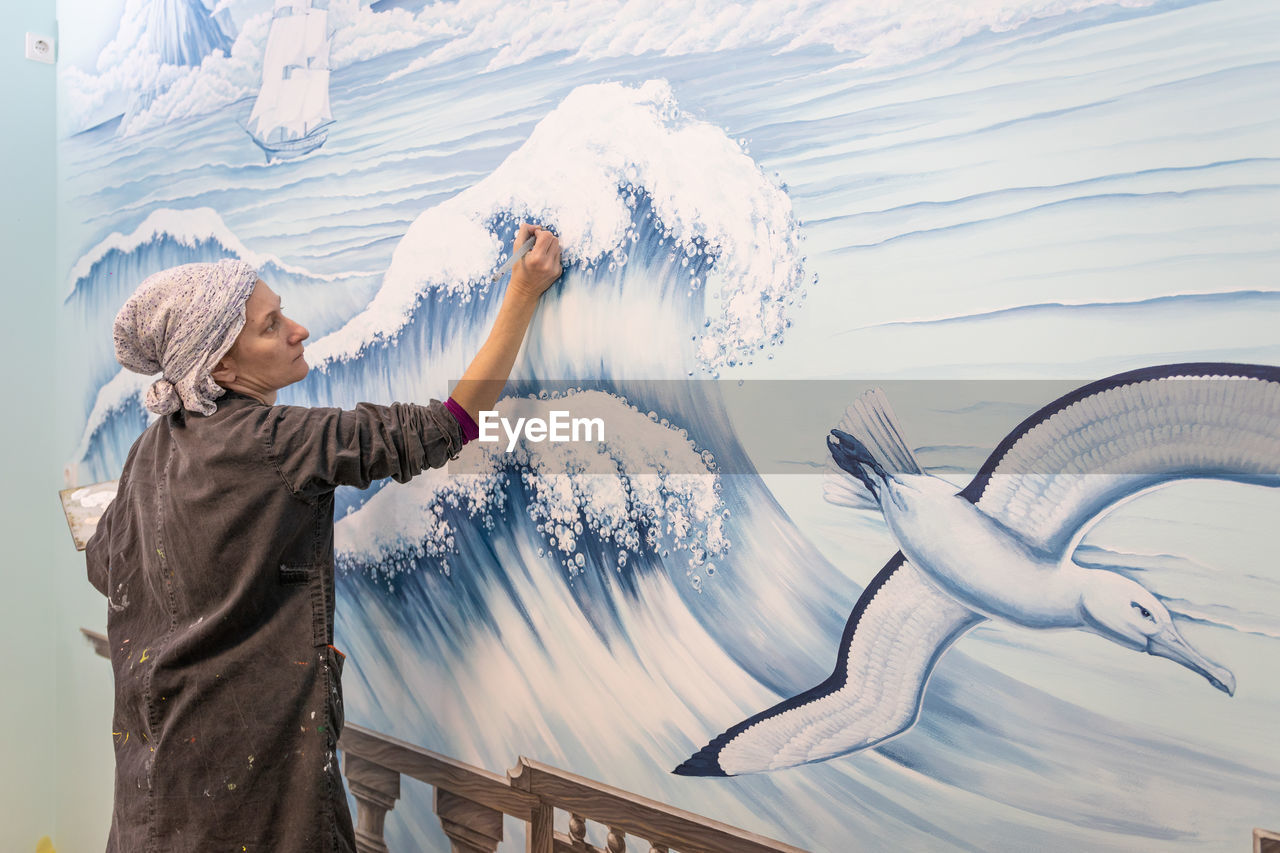 Mature woman artist draws a mural on a marine theme