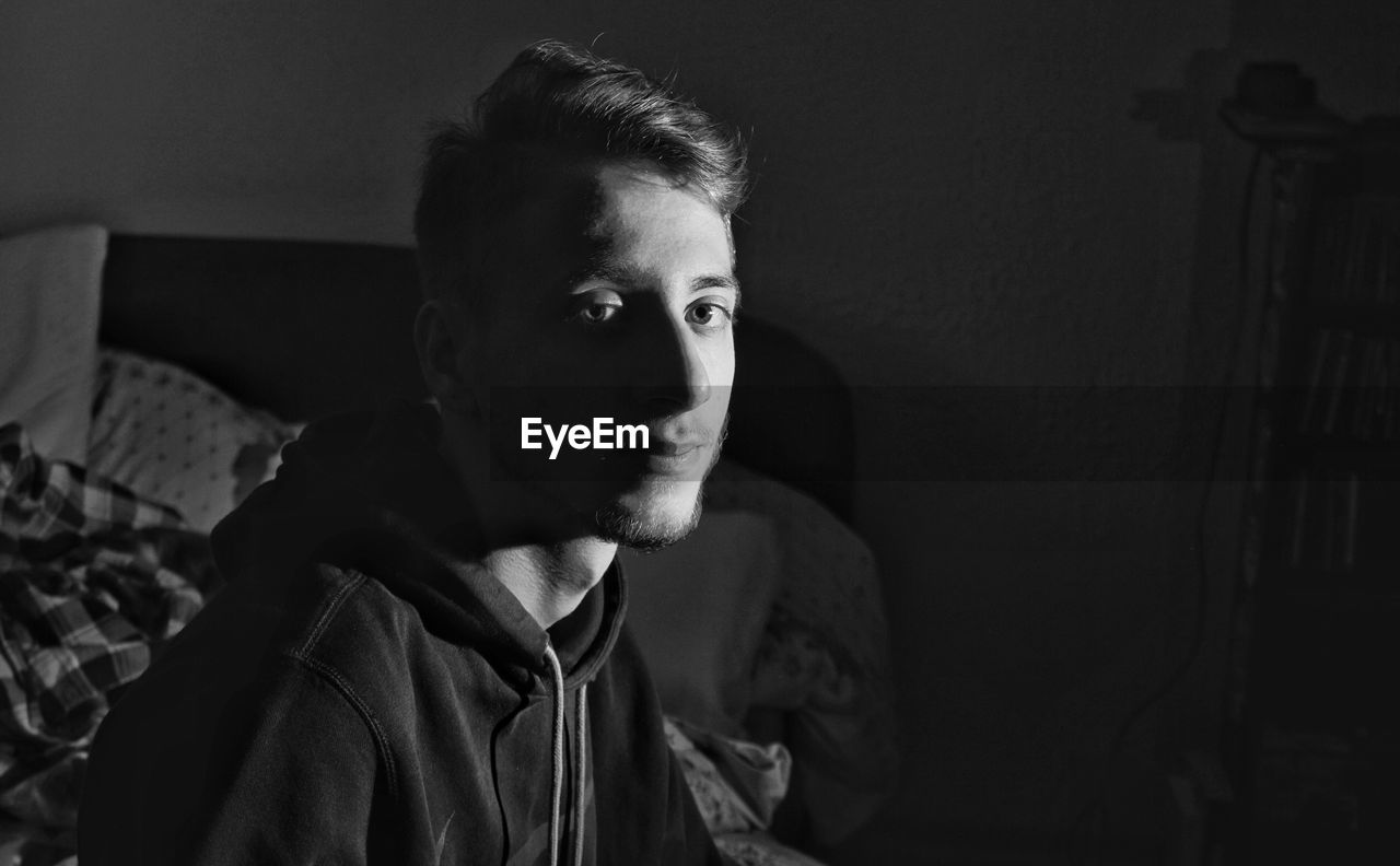 Portrait of young man sitting on bed at home