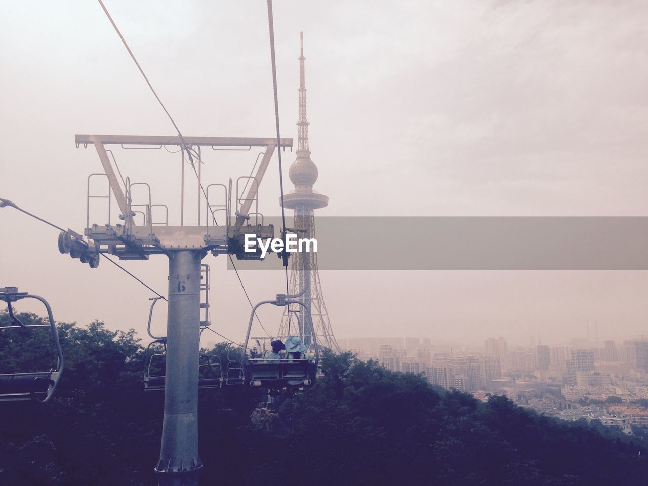 Ski lift towards communication tower in city against sky