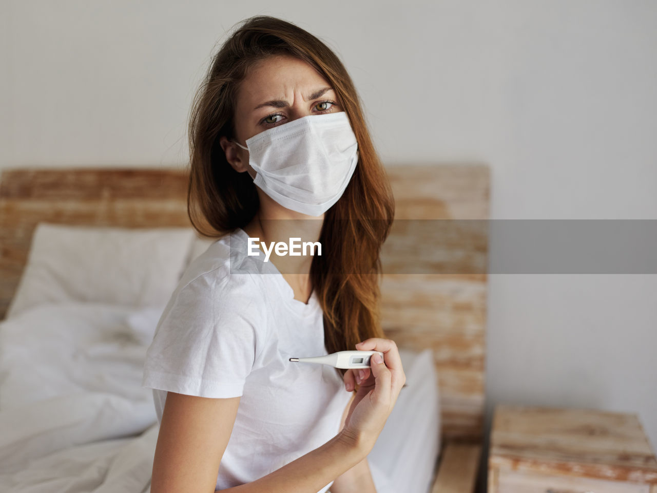 Young woman examining temperature while sitting on bed at home