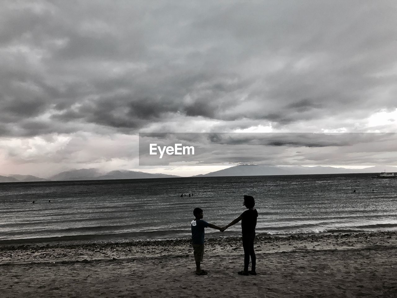 SILHOUETTE FRIENDS STANDING ON BEACH AGAINST SKY