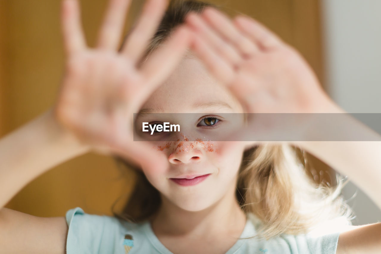 Little girl with glitters on face gesturing while looking at camera in blur