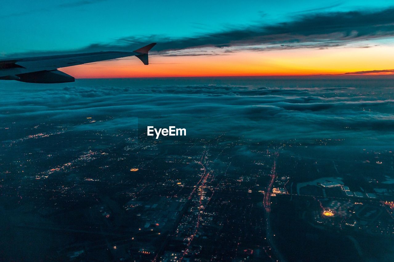 Airplane flying over city during sunset