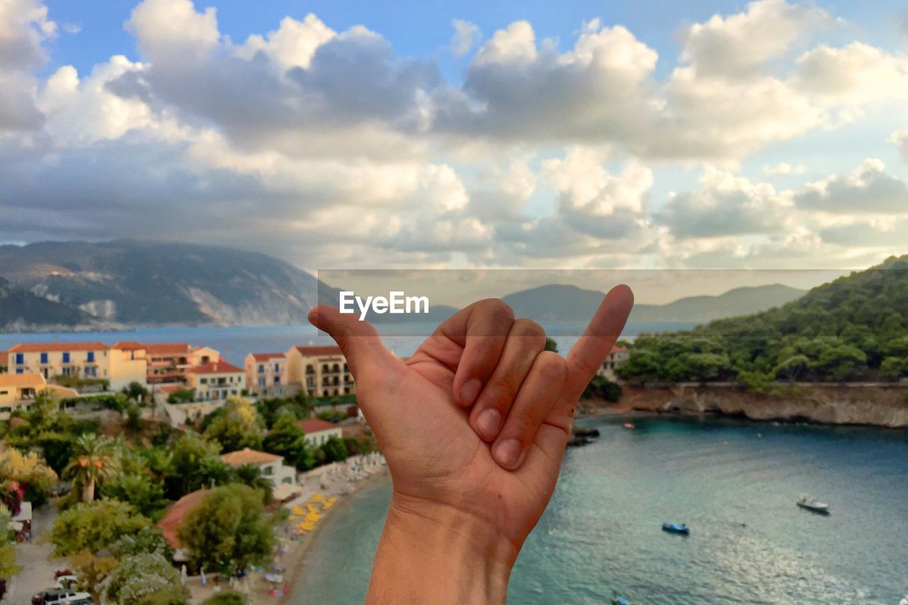 Person gesturing shaka sign by lake against sky