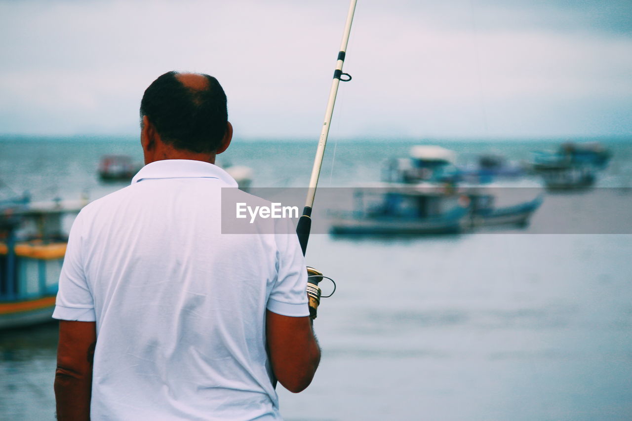 Rear view of man holding sailboat in sea