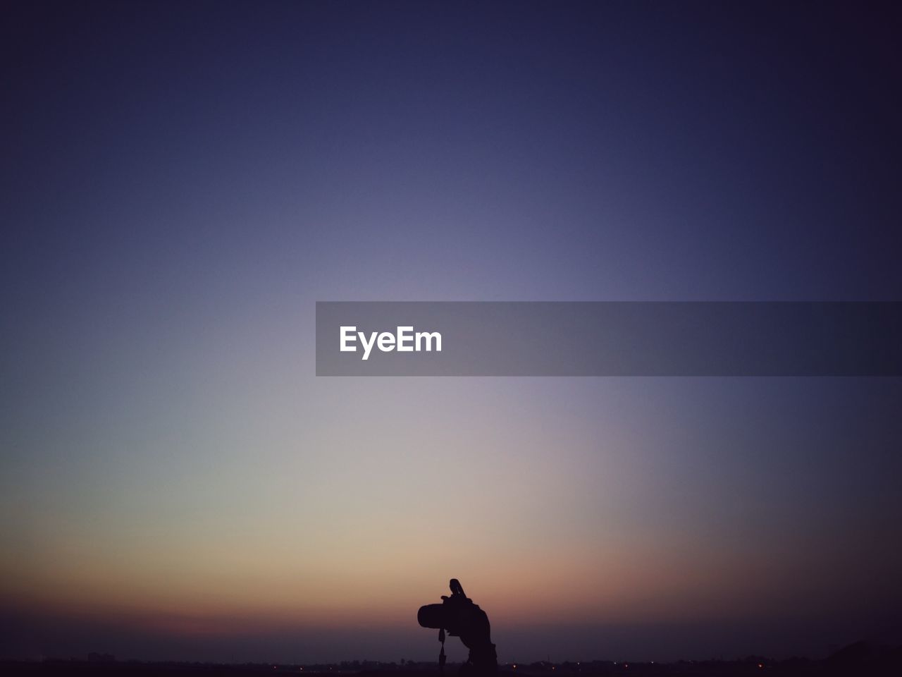 Cropped image of hand holding camera against sky at dusk