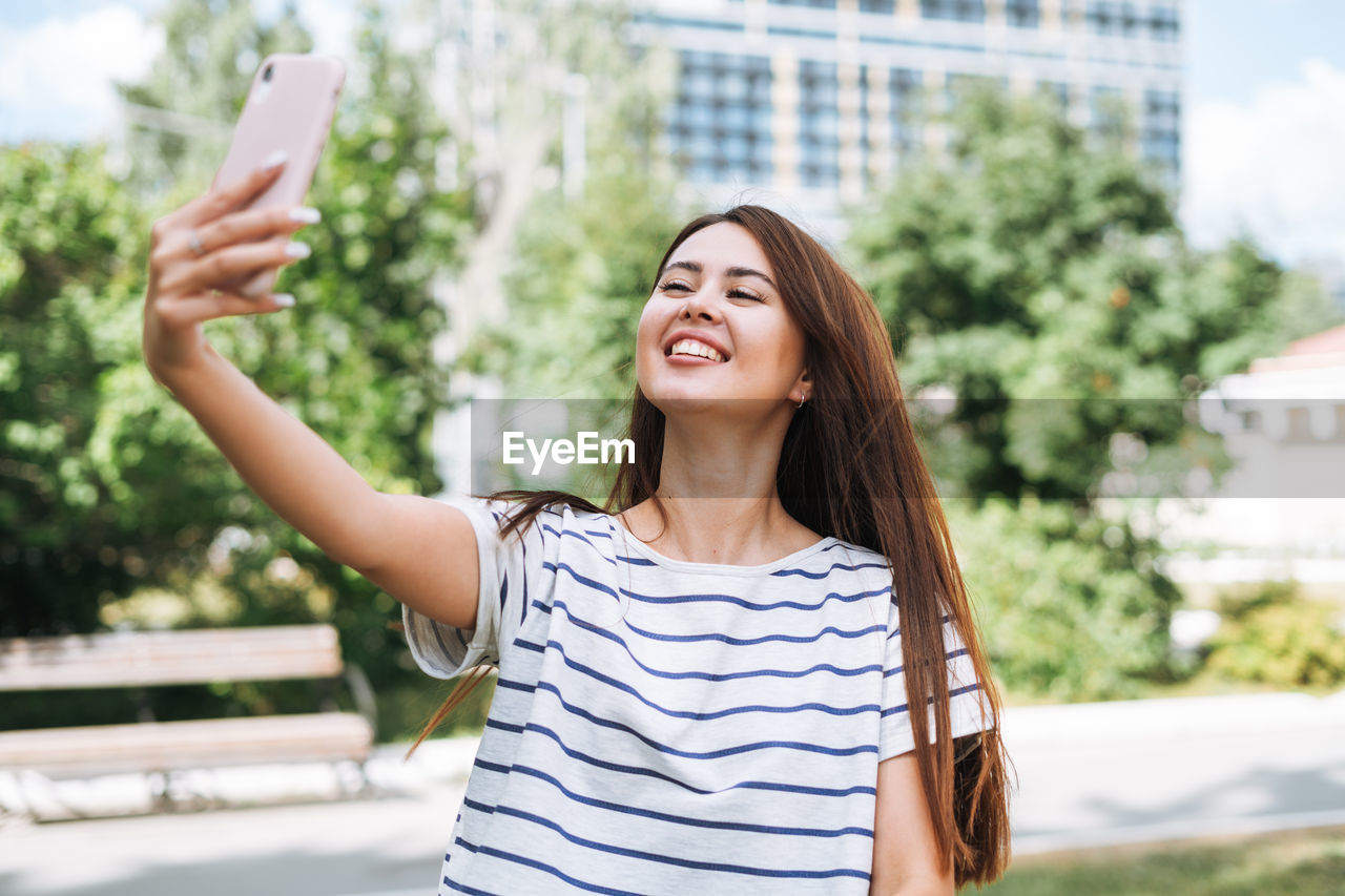 Portrait of young woman student with long hair taking selfie in city park