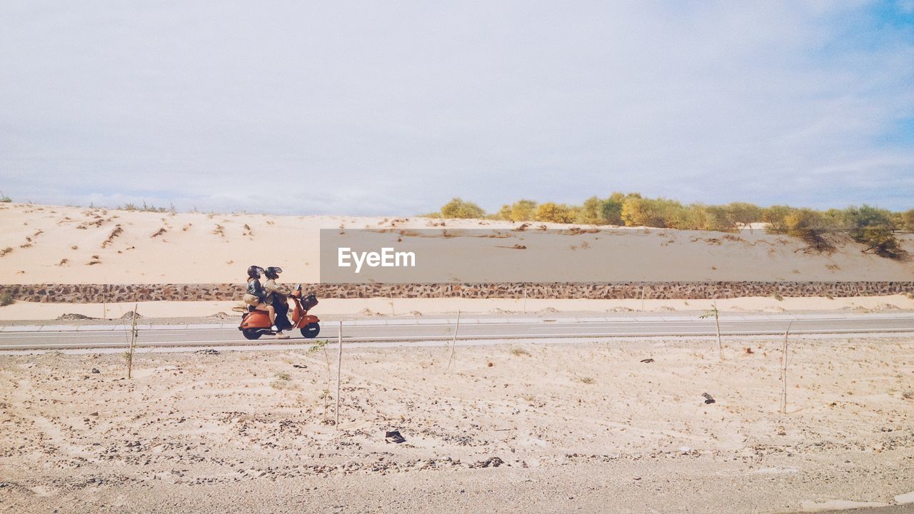 Man and woman riding on scooter in barren landscape