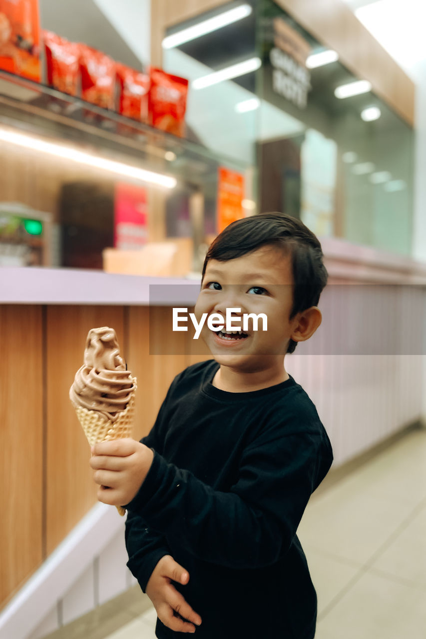 A boy holding ice cream with a happy smile in a cafe