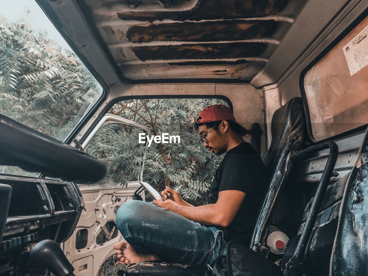 Side view of young man writing on book while sitting in car