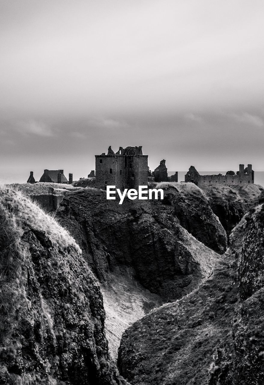 Low angle view of old ruin on rock formation against cloudy sky