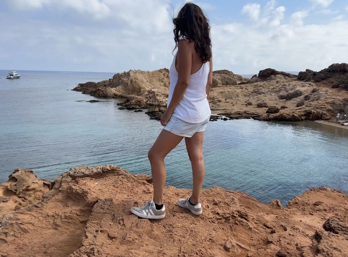 water, one person, sea, land, beach, full length, sky, vacation, coast, rock, nature, adult, shore, women, trip, cloud, ocean, holiday, beauty in nature, leisure activity, sand, young adult, hairstyle, rear view, lifestyles, scenics - nature, long hair, standing, casual clothing, clothing, day, tranquility, travel, body of water, human leg, relaxation, travel destinations, cliff, environment, outdoors, person, summer, coastline, terrain, limb, tourism, fashion, solitude, idyllic, tranquil scene, female, photo shoot, horizon over water, tourist, horizon, brown hair