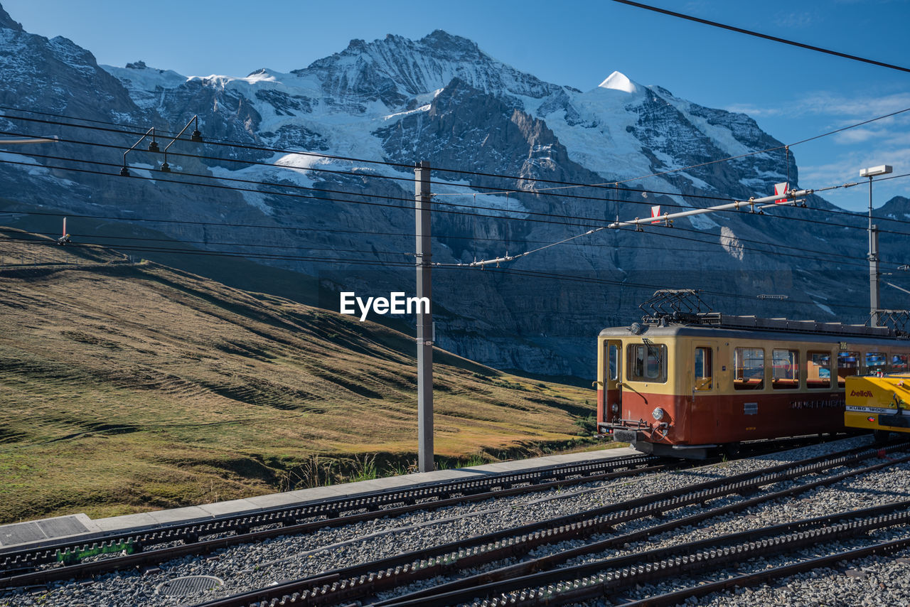 TRAIN ON RAILROAD TRACKS AGAINST SNOWCAPPED MOUNTAINS