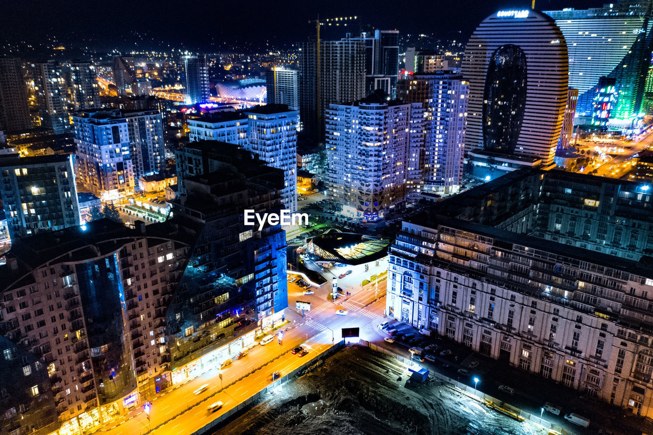 HIGH ANGLE VIEW OF ILLUMINATED STREET AMIDST BUILDINGS IN CITY