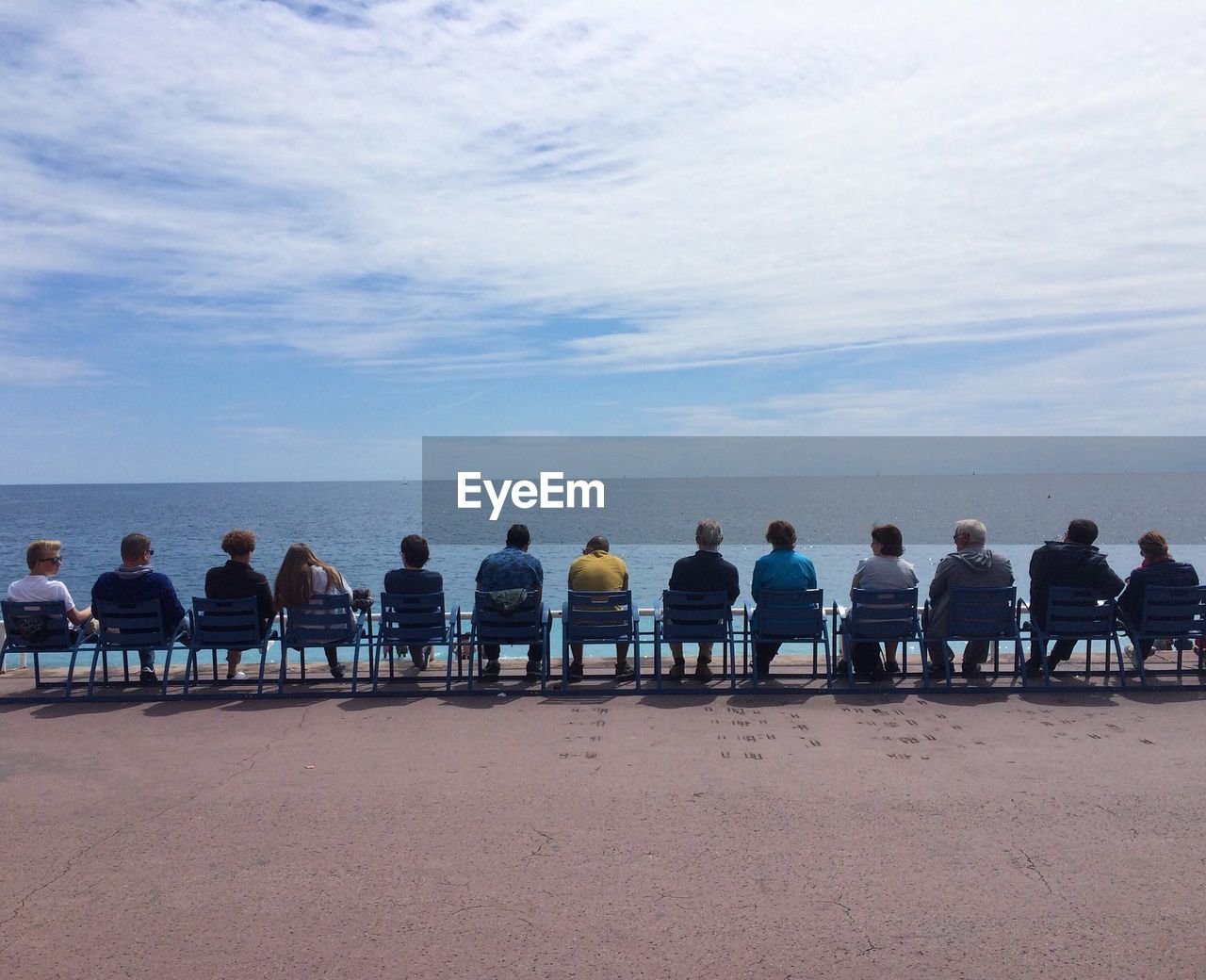 People sitting on chairs by sea against sky