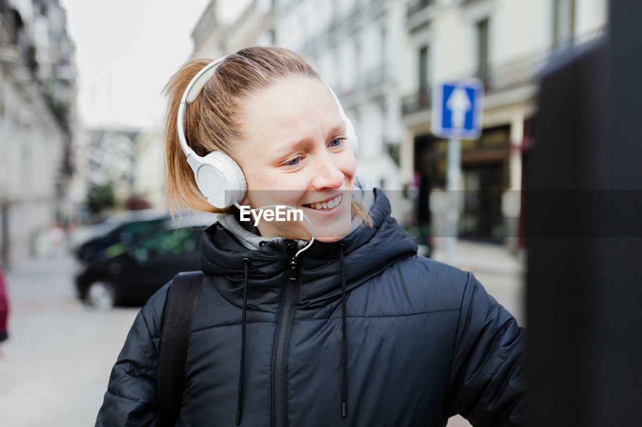 Smiling young woman listening to music using parking meter in city