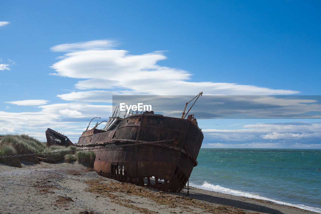 ABANDONED BOAT ON SHORE AGAINST SKY